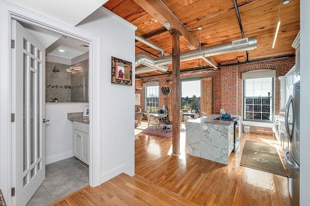 interior space featuring beam ceiling, light wood-type flooring, wood ceiling, and brick wall