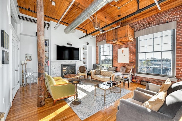 living room with beam ceiling, wooden ceiling, a high ceiling, a premium fireplace, and brick wall