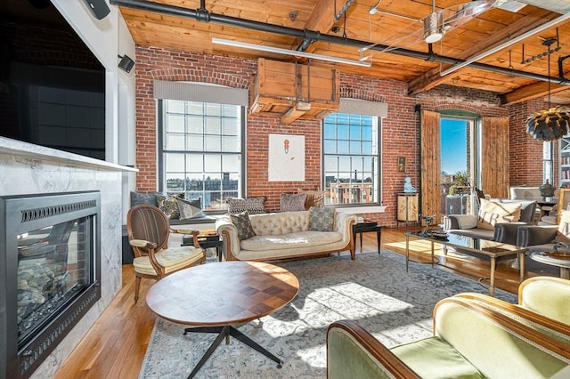 living room featuring beam ceiling, light hardwood / wood-style flooring, brick wall, and a high ceiling