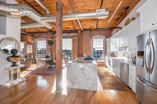 kitchen featuring light wood-type flooring, light stone counters, brick wall, stainless steel appliances, and white cabinetry