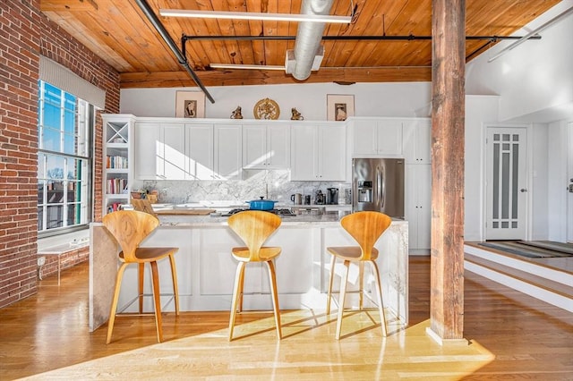 kitchen featuring backsplash, white cabinets, appliances with stainless steel finishes, a breakfast bar area, and brick wall