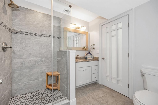 bathroom featuring tile patterned floors, toilet, vanity, and tiled shower