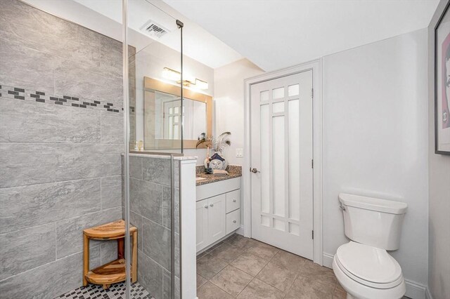 bathroom with a tile shower, tile patterned floors, vanity, and toilet