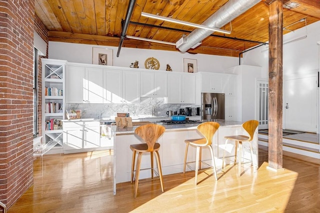 kitchen with stainless steel refrigerator with ice dispenser, backsplash, wooden ceiling, white cabinets, and a kitchen island