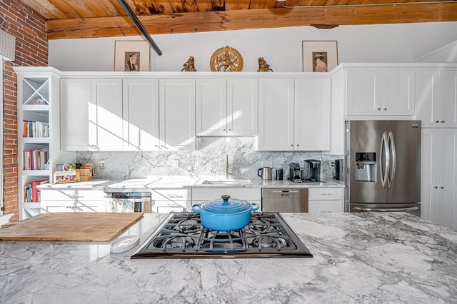 kitchen with light stone counters, brick wall, stainless steel appliances, sink, and beam ceiling