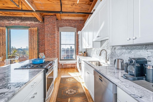 kitchen with brick wall, stainless steel appliances, sink, wooden ceiling, and beamed ceiling