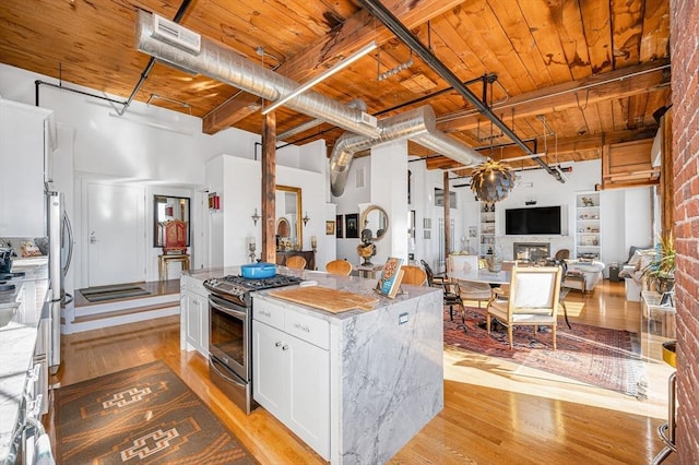 kitchen with a towering ceiling, light stone counters, stainless steel appliances, white cabinets, and a kitchen island