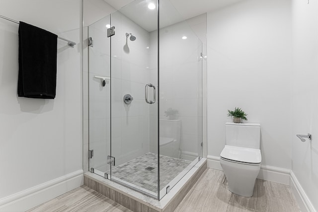 bathroom with toilet, a shower with shower door, and hardwood / wood-style floors