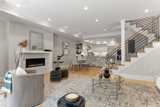 living room with light wood-type flooring, a tray ceiling, a tile fireplace, and crown molding