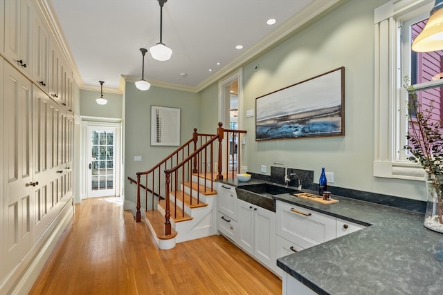 interior space featuring crown molding, light hardwood / wood-style flooring, sink, hanging light fixtures, and white cabinets