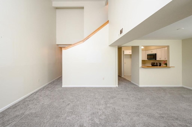unfurnished living room featuring light colored carpet, baseboards, a towering ceiling, and visible vents