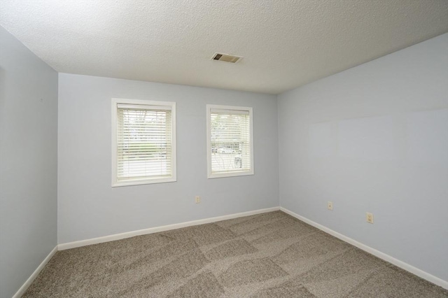 carpeted empty room with baseboards, a textured ceiling, and visible vents