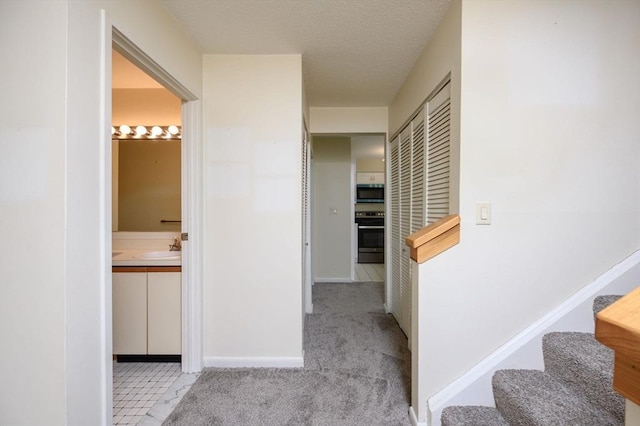 corridor featuring stairs, baseboards, carpet floors, and a sink