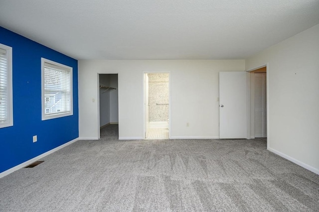unfurnished bedroom with baseboards, carpet, a spacious closet, and visible vents
