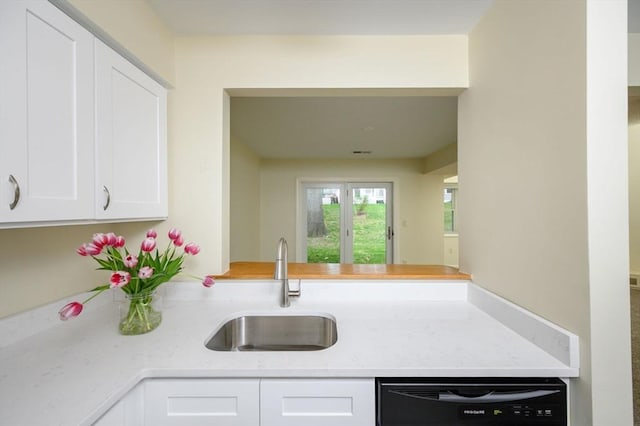 kitchen featuring a peninsula, light stone countertops, black dishwasher, white cabinets, and a sink