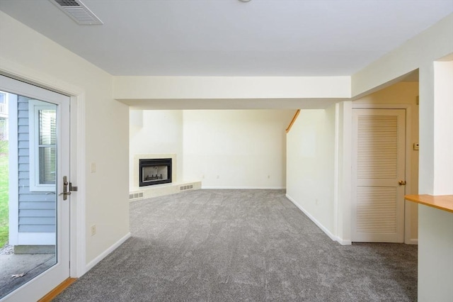 unfurnished living room with a fireplace with raised hearth, carpet flooring, and visible vents