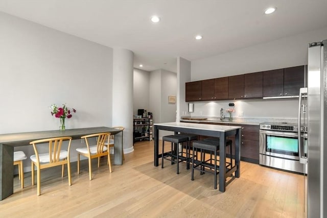 kitchen featuring recessed lighting, light countertops, appliances with stainless steel finishes, dark brown cabinetry, and light wood-type flooring