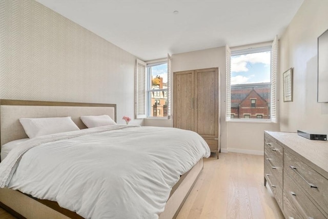 bedroom with an accent wall, light wood-style floors, and baseboards