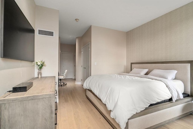 bedroom featuring baseboards, an accent wall, visible vents, and light wood-style floors