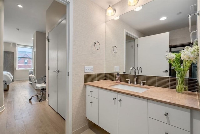 ensuite bathroom with backsplash, hardwood / wood-style floors, ensuite bath, and vanity