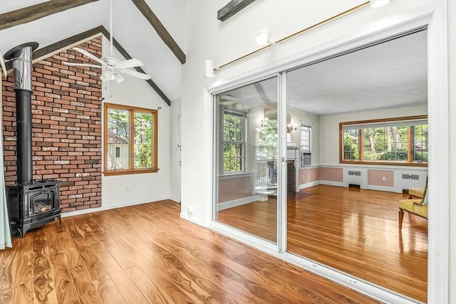 unfurnished living room featuring ceiling fan, wood finished floors, a wood stove, baseboards, and radiator