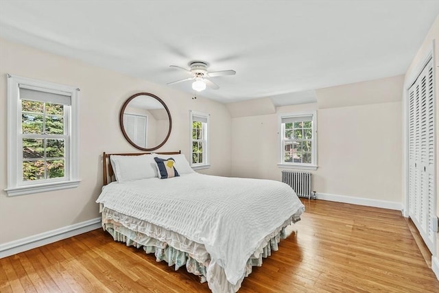 bedroom featuring radiator, baseboards, light wood finished floors, and a ceiling fan