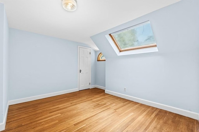 bonus room with a skylight, light wood-type flooring, baseboards, and vaulted ceiling