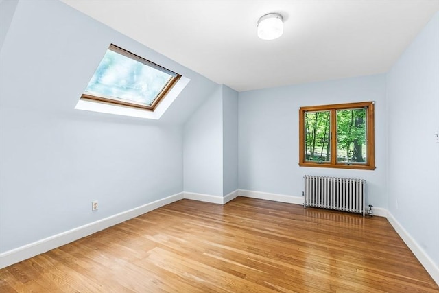 additional living space with radiator, light wood-type flooring, a skylight, baseboards, and lofted ceiling
