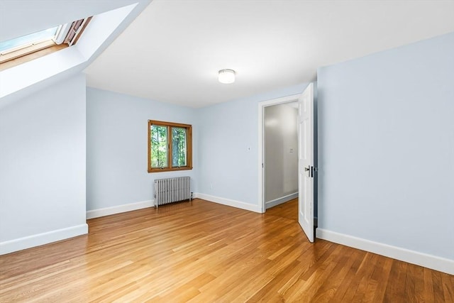additional living space with radiator heating unit, a skylight, light wood-style floors, and baseboards