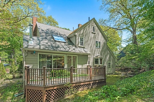 back of house with a chimney, a deck, and roof with shingles