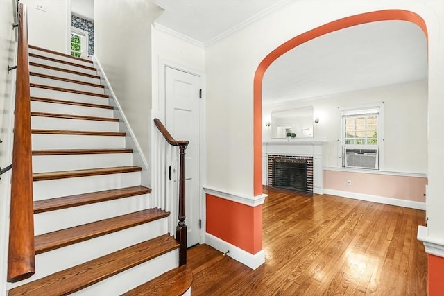 stairway featuring arched walkways, wood finished floors, baseboards, ornamental molding, and a brick fireplace