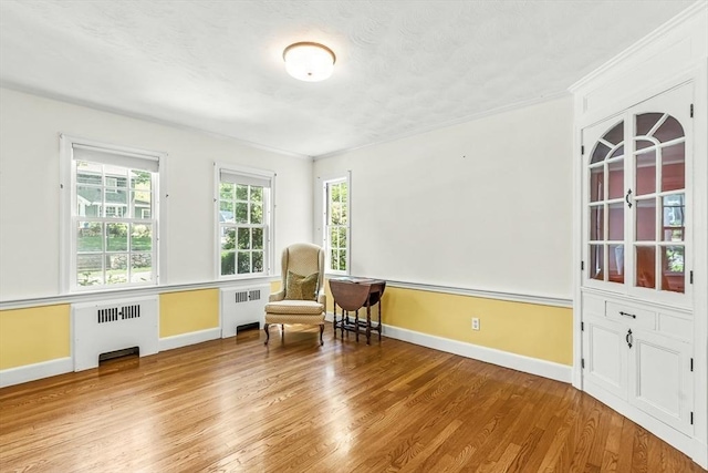living area with radiator heating unit, wood finished floors, baseboards, and ornamental molding
