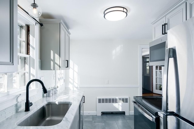 kitchen featuring radiator, sink, dark tile patterned floors, appliances with stainless steel finishes, and light stone countertops