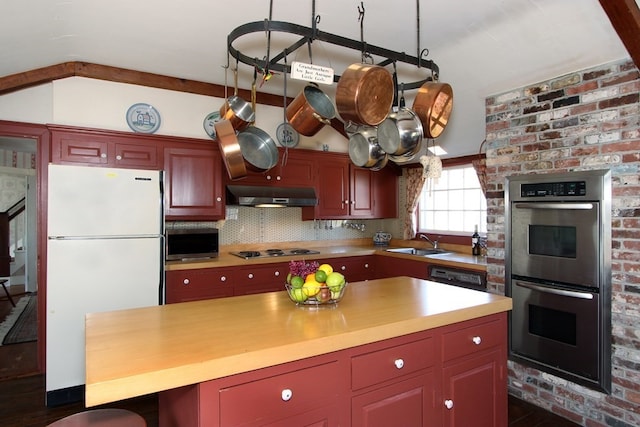 kitchen with appliances with stainless steel finishes, brick wall, fume extractor, sink, and tasteful backsplash