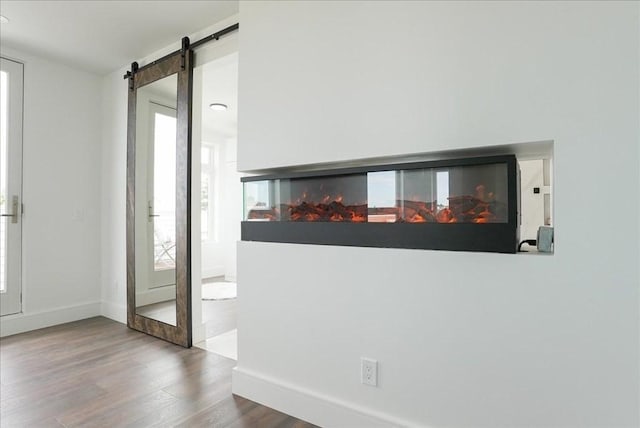 interior space with a wealth of natural light, a barn door, wood finished floors, and baseboards