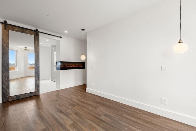 empty room with recessed lighting, a barn door, baseboards, and wood finished floors
