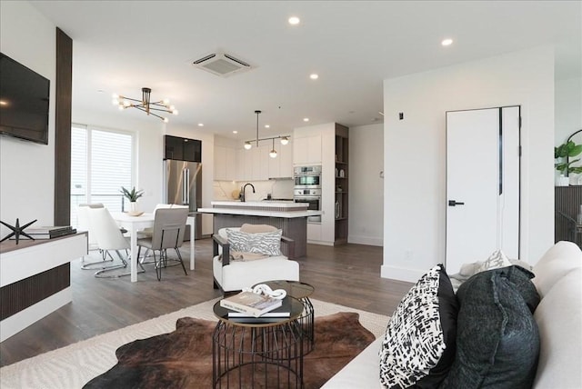 living room featuring visible vents, baseboards, a chandelier, recessed lighting, and wood finished floors