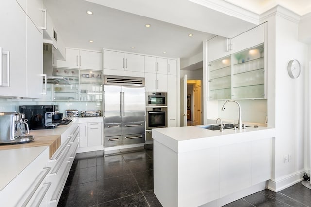 kitchen with appliances with stainless steel finishes, white cabinets, wall chimney exhaust hood, dark tile flooring, and sink