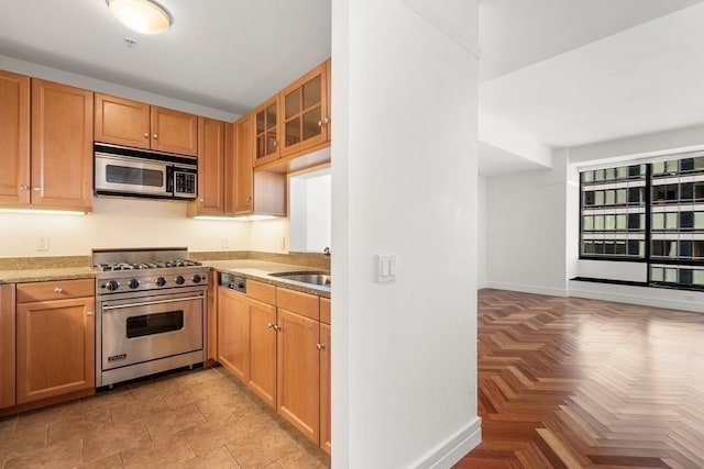 kitchen with light parquet flooring, stainless steel appliances, sink, and light stone countertops