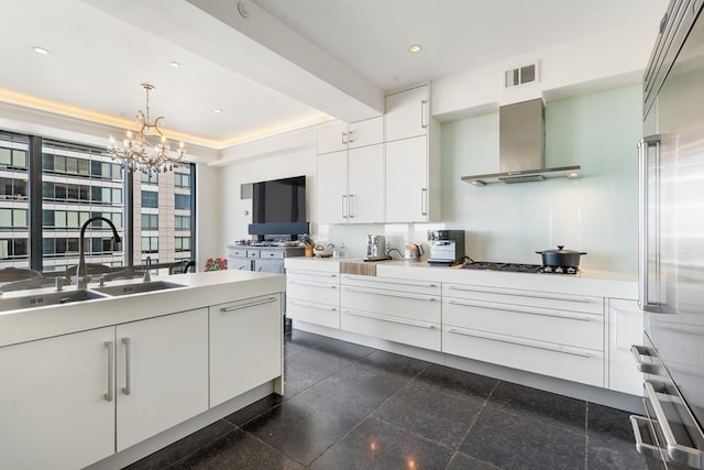 kitchen featuring decorative light fixtures, white cabinetry, a notable chandelier, sink, and wall chimney exhaust hood