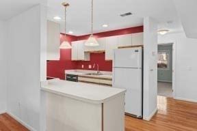 kitchen with hanging light fixtures, light countertops, light wood-style flooring, freestanding refrigerator, and baseboards