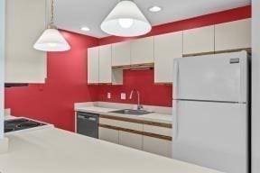 kitchen featuring a sink, light countertops, freestanding refrigerator, and dishwasher