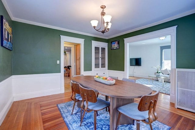 dining space with crown molding, an inviting chandelier, and light wood-type flooring