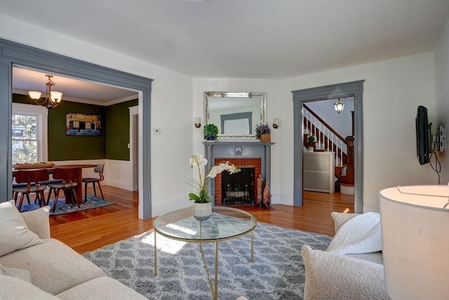 living room featuring a notable chandelier, crown molding, a fireplace, and wood-type flooring