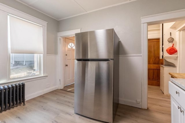 kitchen featuring radiator, white cabinets, light hardwood / wood-style flooring, stainless steel fridge, and ornamental molding