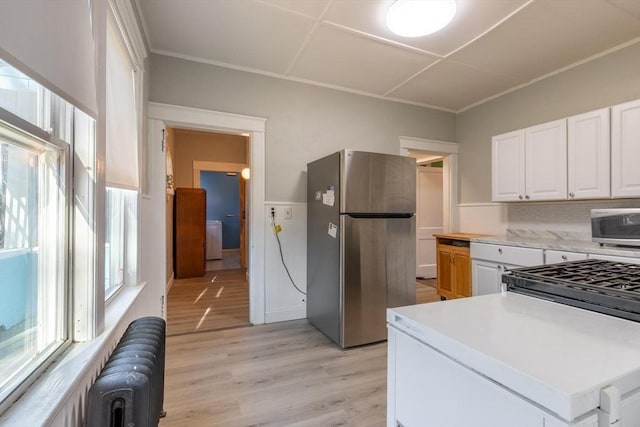 kitchen with white cabinets, light wood-type flooring, tasteful backsplash, radiator heating unit, and stainless steel appliances