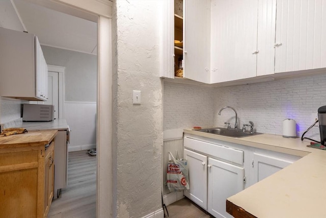 kitchen with white cabinets, backsplash, light hardwood / wood-style floors, and sink