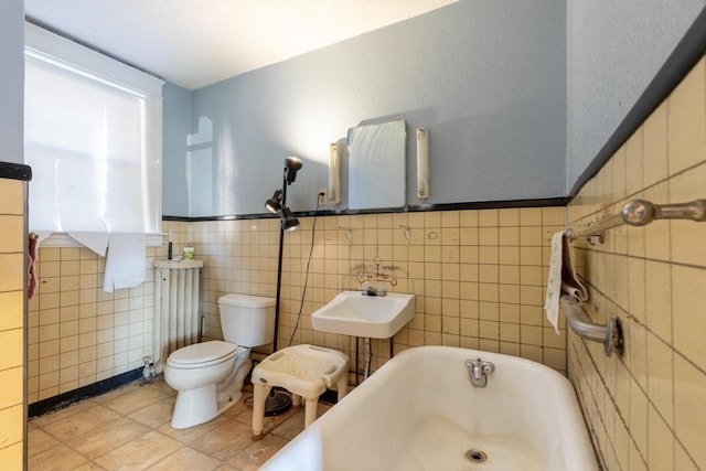 bathroom with tile patterned floors, sink, a bath, tile walls, and toilet