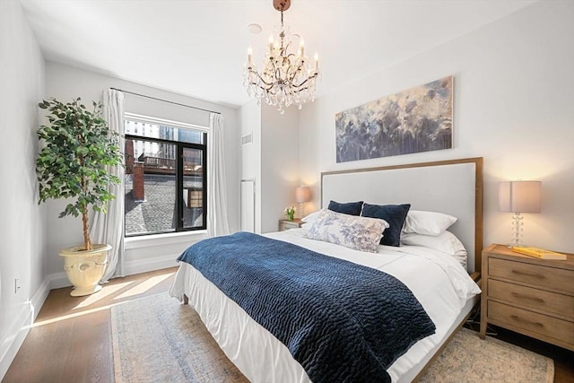 bedroom with baseboards, wood finished floors, and a notable chandelier