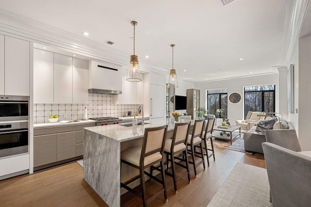 kitchen featuring crown molding, a sink, open floor plan, light wood-style floors, and a breakfast bar